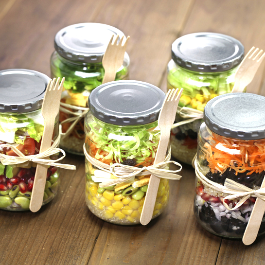 Chopped veggies for salad in glass jars with wooden fork.