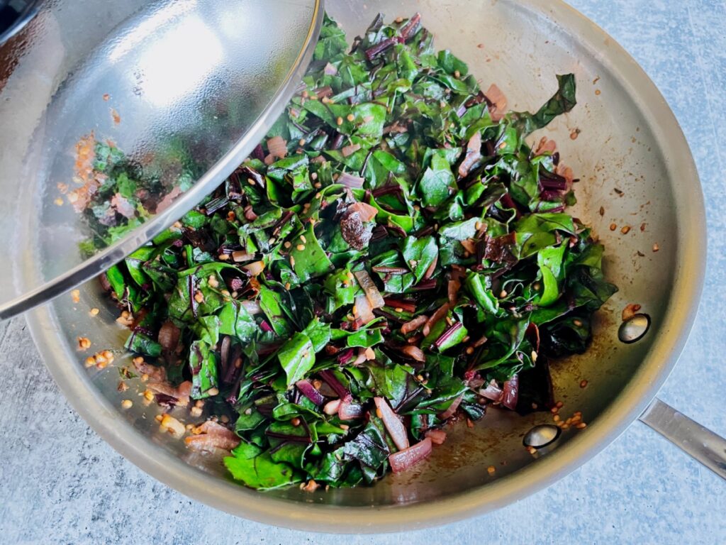 Beetroot greens, onion and urad dal in pan and lid.