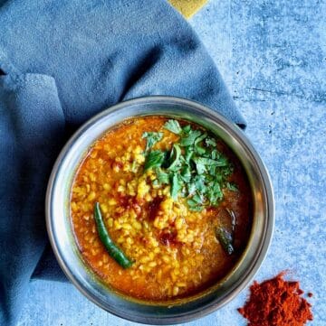 Bengali Moong Dal or Bhaja Moonger Daal in bowl, kashmiri chili powder on the lower right and grey and mustard-colred towels underneath.