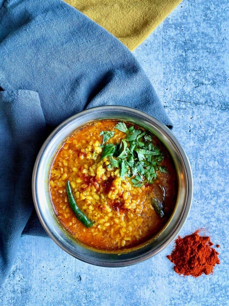 Bengali Moong Dal or Bhaja Moonger Daal in bowl, chili powder on the lower right and towels underneath.