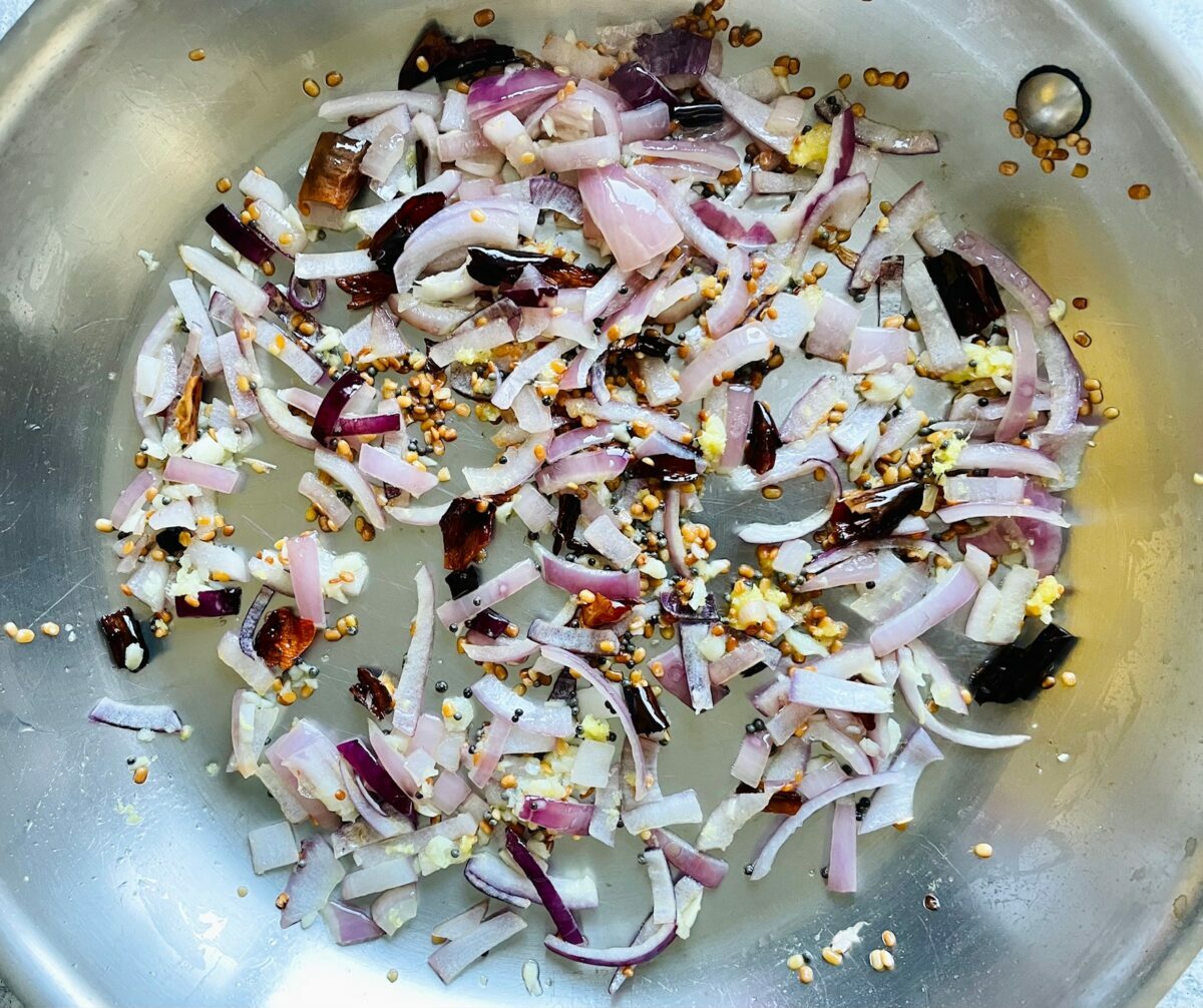 Onion and spices in stainless steel pan.