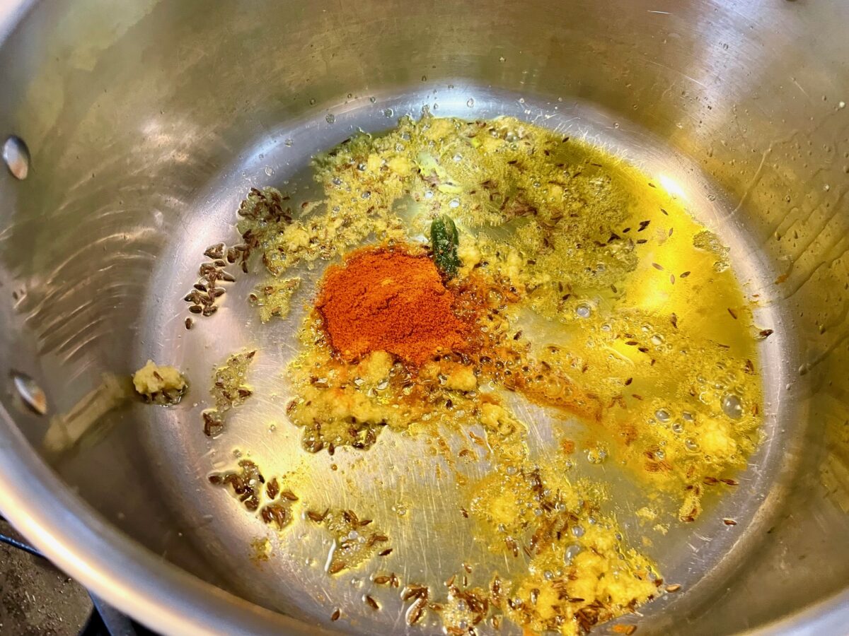 Cumin seeds, turmeric, chili powder, ghee and grated ginger for Bengali moong dal cooking in pot.