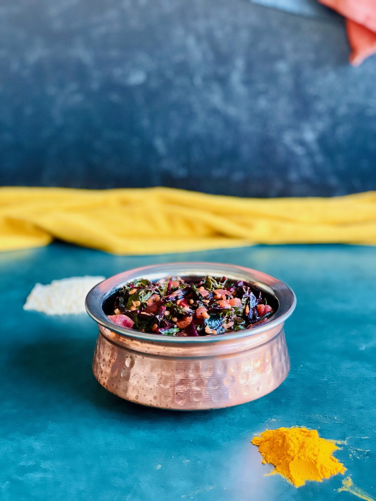 Vegan beetroot leaves in copper bowl, turmeric powder in front and urad dal in the back.