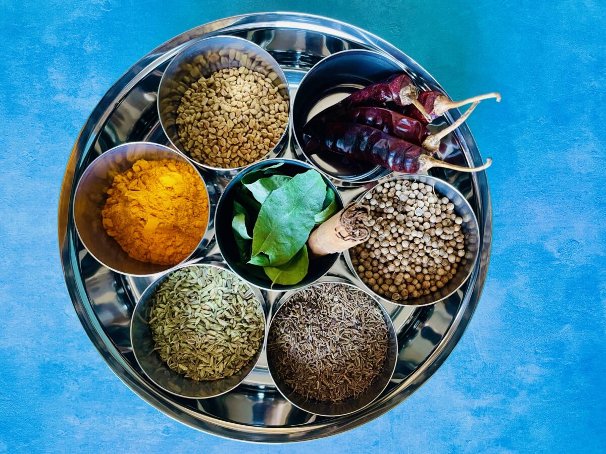 Ingredients for Mauritian curry powder in stainless steel bowls: coriander seeds, cumin seeds, fennel seeds, red chilies, cinnamon stick, curry leaves and turmeric powder.