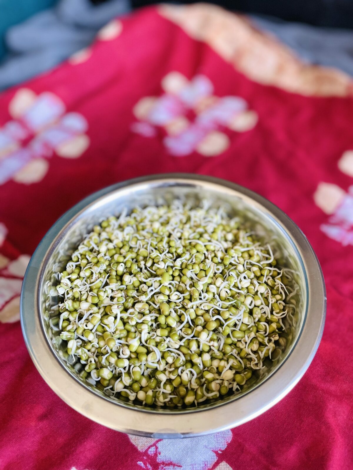 Sprouted moong dal in stainless steel bowl on red cloth.