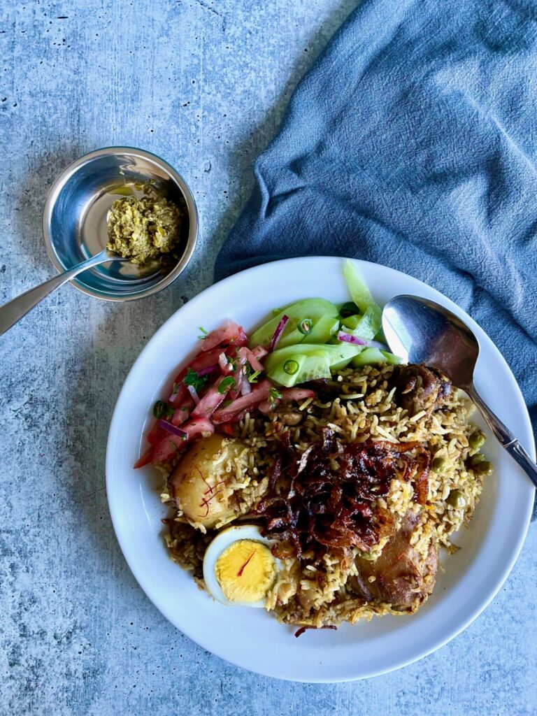 Plate of chicken biryani cooked with ghee. Green chili paste in bowl (condiment).