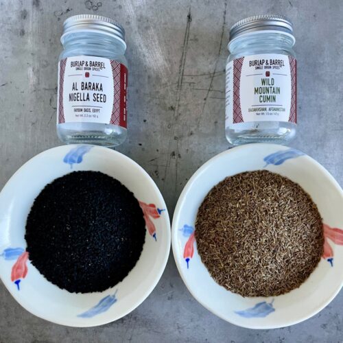 Black Cumin vs Wild Cumin in bowls and their empty jars. AKA Nigella seeds vs Cumin